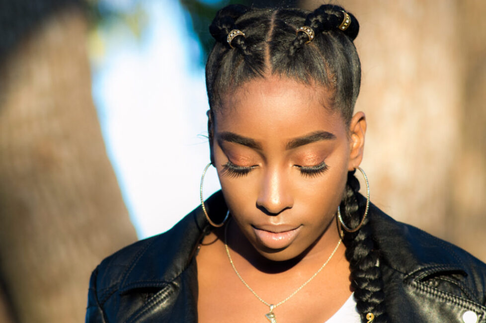 Young woman with braided hair and hoop earrings looking down.