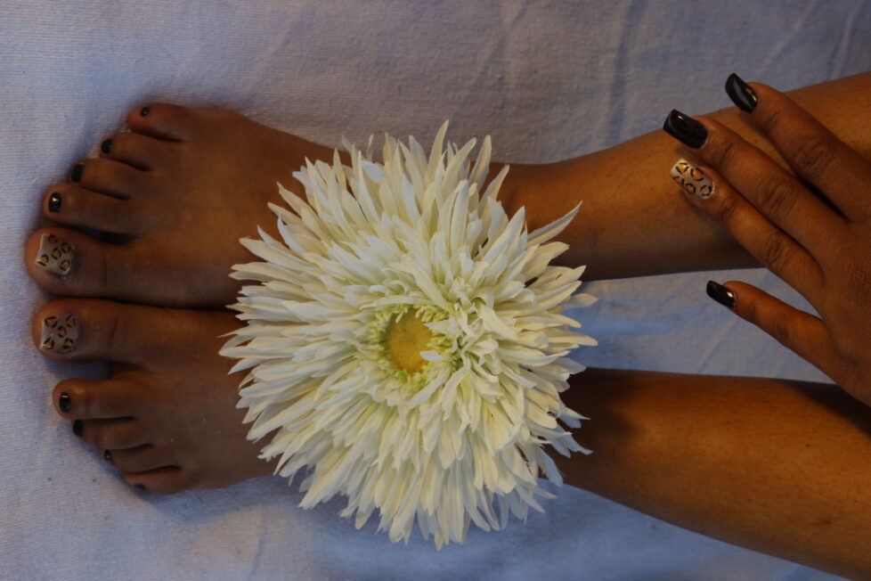 White flower placed between bare feet against a plain background.